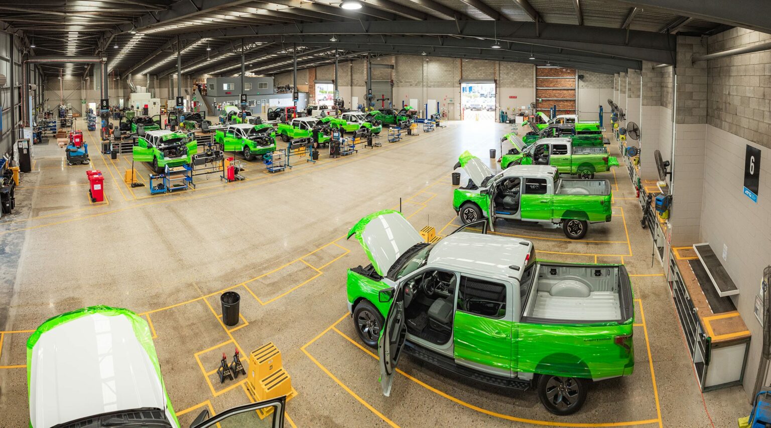 AUSEV - A panoramic view of a bright, busy car assembly line with workers actively engaging in the manufacturing process of vibrant green F-150 Lightning trucks.