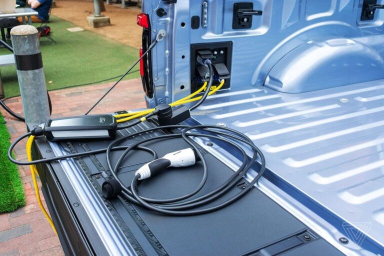 AUSEV - An electric vehicle charger is placed in the trunk of a blue F-150 Lightning, connected to a built-in charging port, with cables neatly arranged on the metal surface.